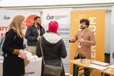 Zwei Männer und eine Frau sprechen an einem Informationsstand zum Thema Integration und Frauenförderung.