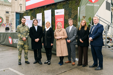 Gruppierung von Personen in formeller Kleidung, Fotografiert vor Bannern zur Integration in Österreich.