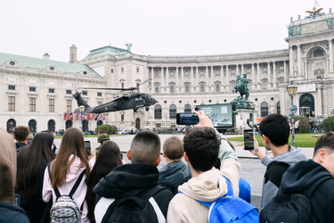 Eine Gruppe von Menschen beobachtet einen Hubschrauber über einem historischen Gebäude.